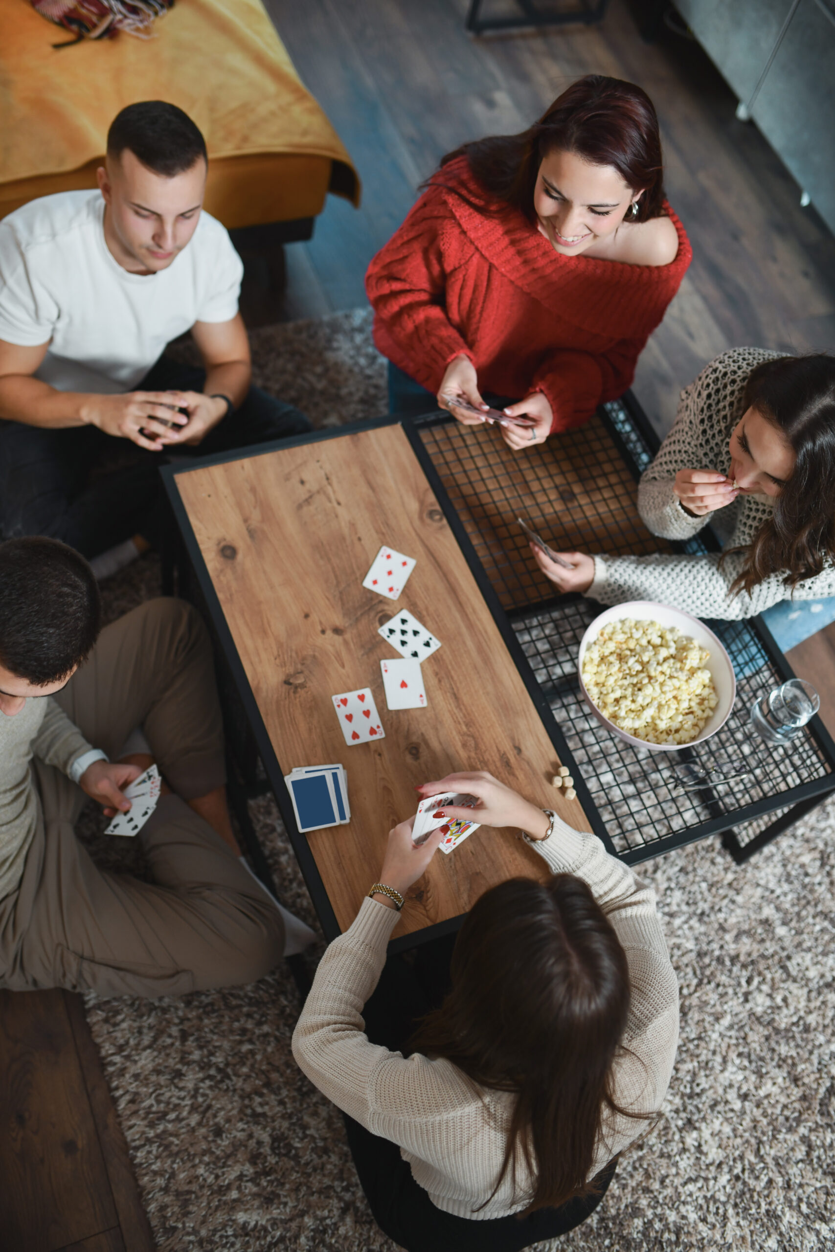 Friends Sitting in Circle Around Coffee Table Playing Card Games and Eating Popcorn